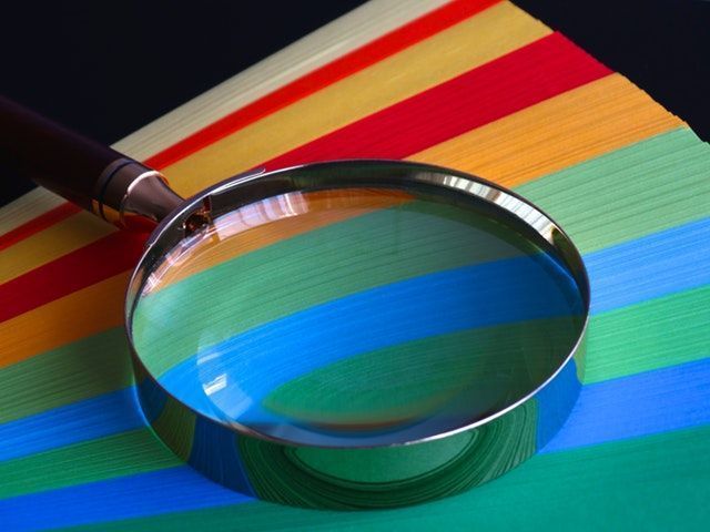 Lupa sobre documentos de colores para hablar de calidad y revisión de los datos